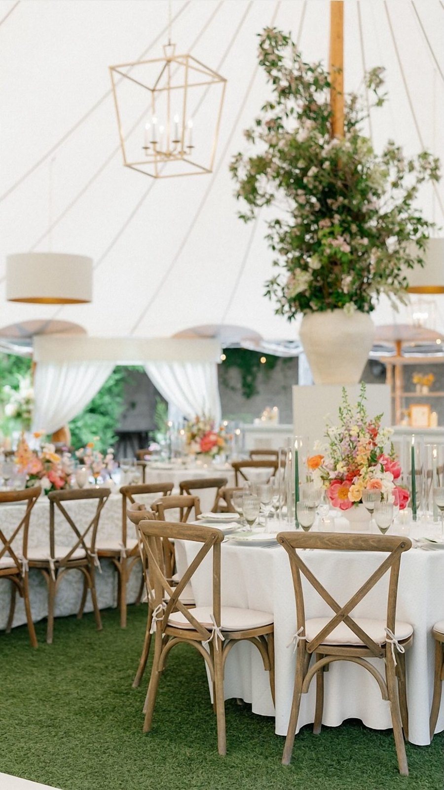 Flowering branch arrangements on white pedestals wrapping the poles of a sailcloth tent