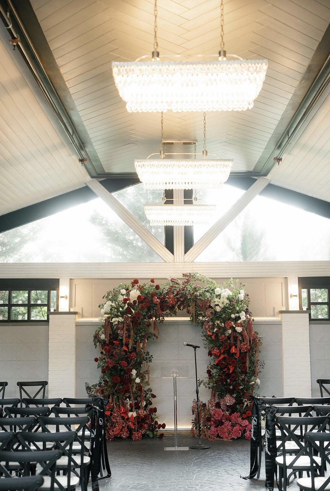Red and white floral ceremony arch beneath tiered crystal chandeliers