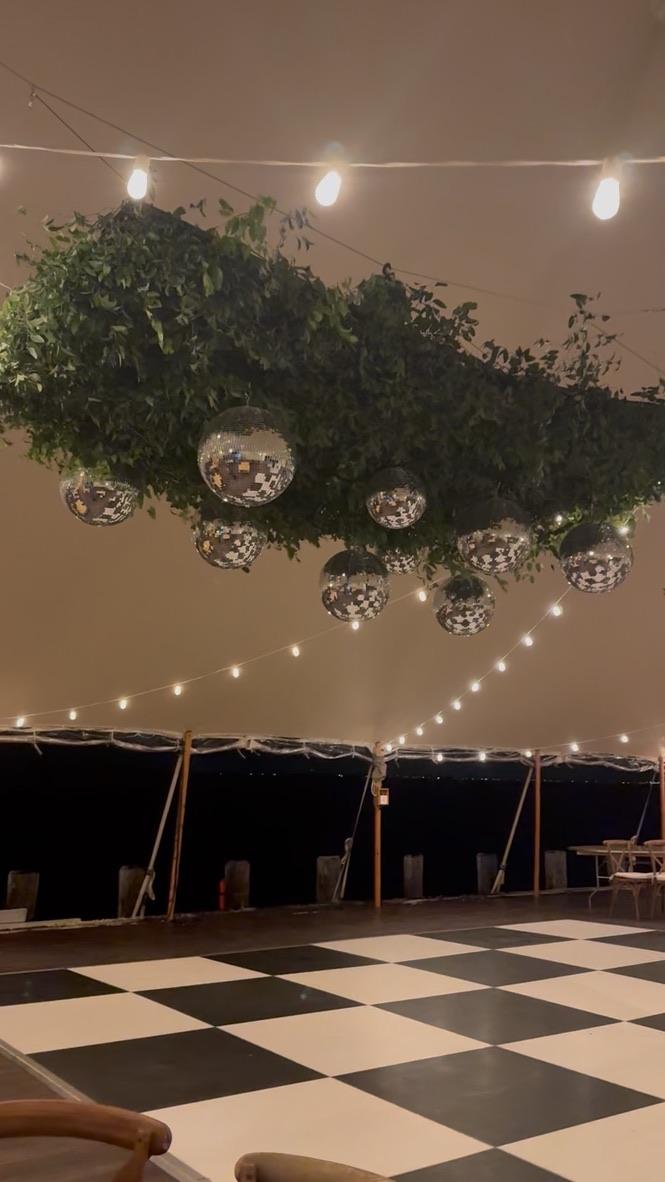 Suspended greenery cloud with hanging disco balls over a black and white dance floor in a sailcloth tent at night