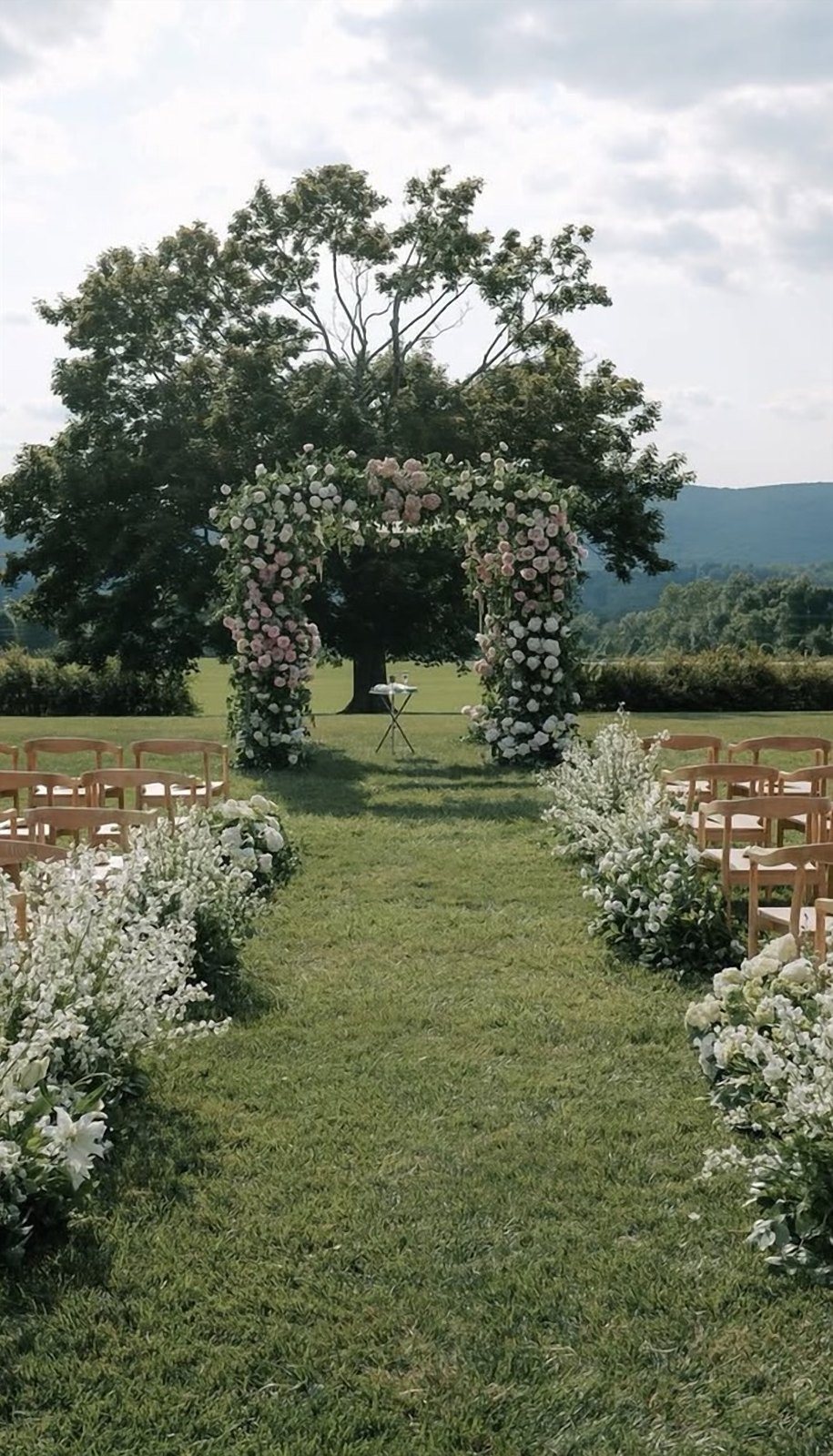 Pink and white floral chuppah on a hilltop lawn with flowering aisle arrangements