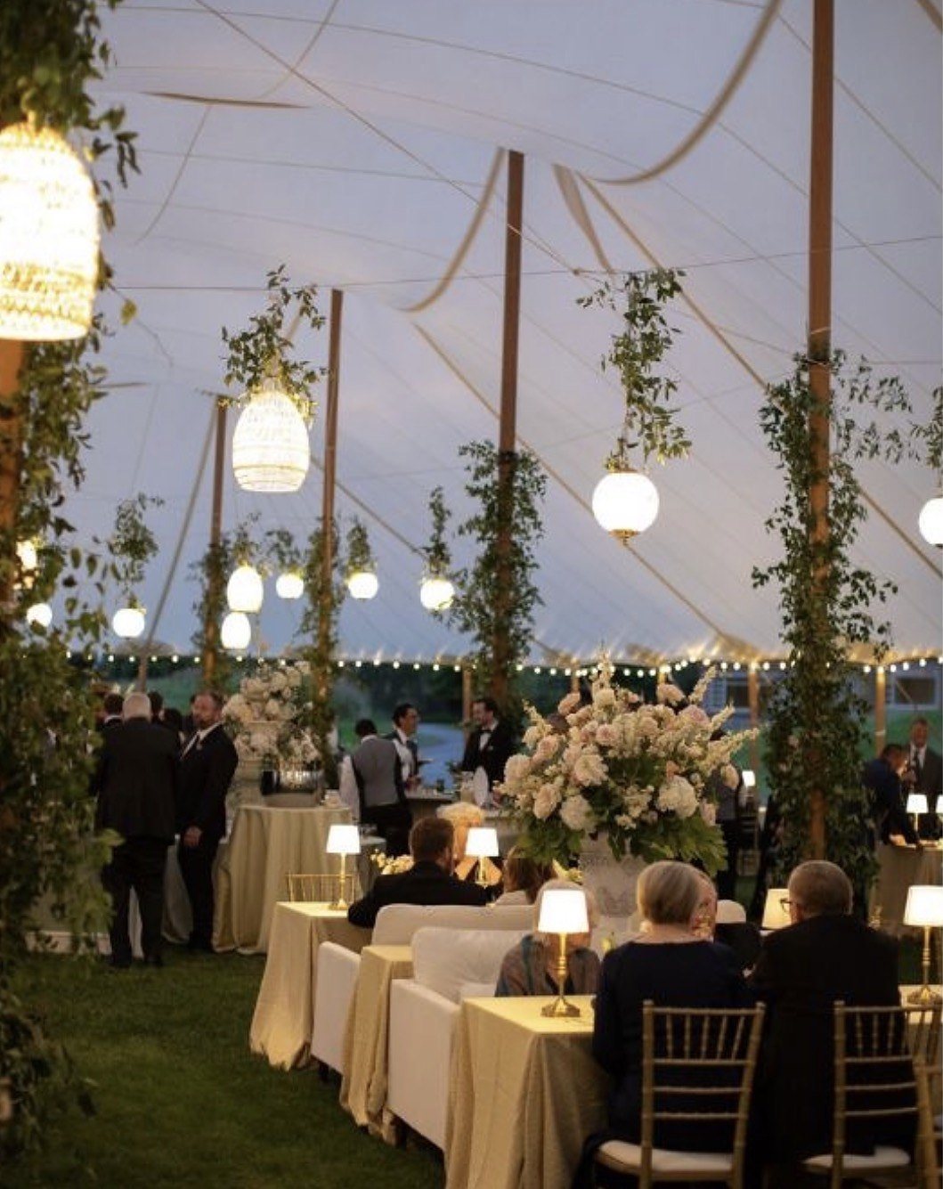 Sailcloth tent at dusk with rigged chandeliers, rattan lanterns and greenery-wrapped poles