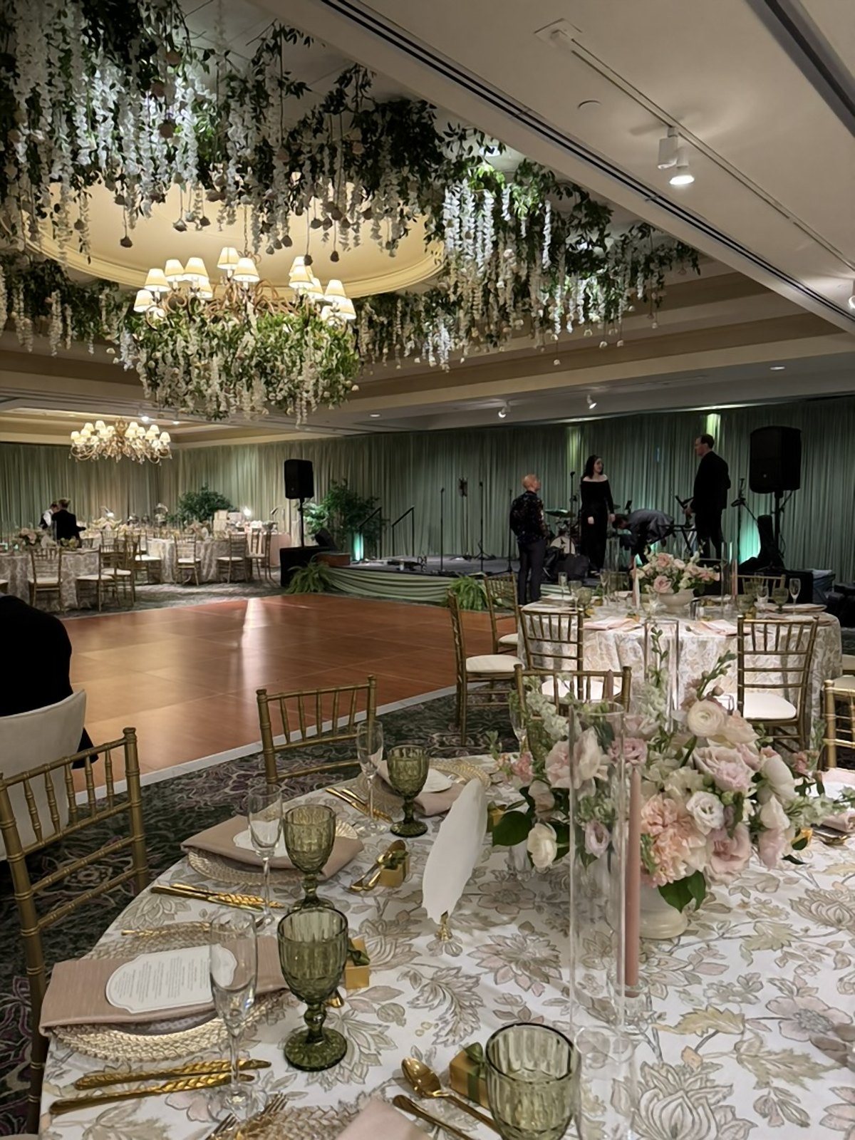 Ballroom with a suspended greenery and floral ceiling around the chandelier, set for a reception