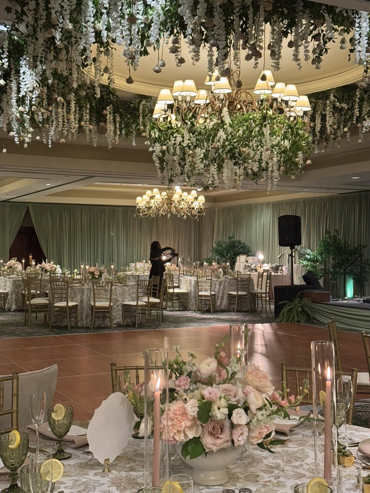 Suspended wisteria and greenery ceiling surrounding a ballroom chandelier above a dance floor