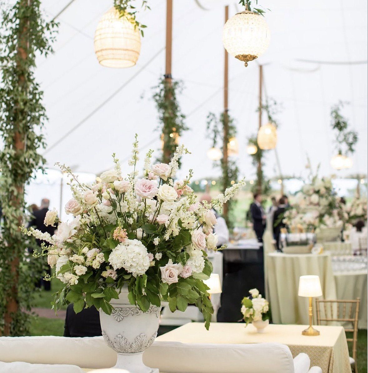Tented reception with an urn arrangement beneath rigged rattan lanterns and a crystal chandelier